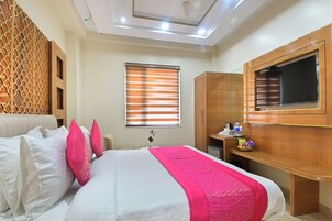 Quarto de hotel com cama, guarda-roupa de madeira, secretária com televisão e janela com persianas.