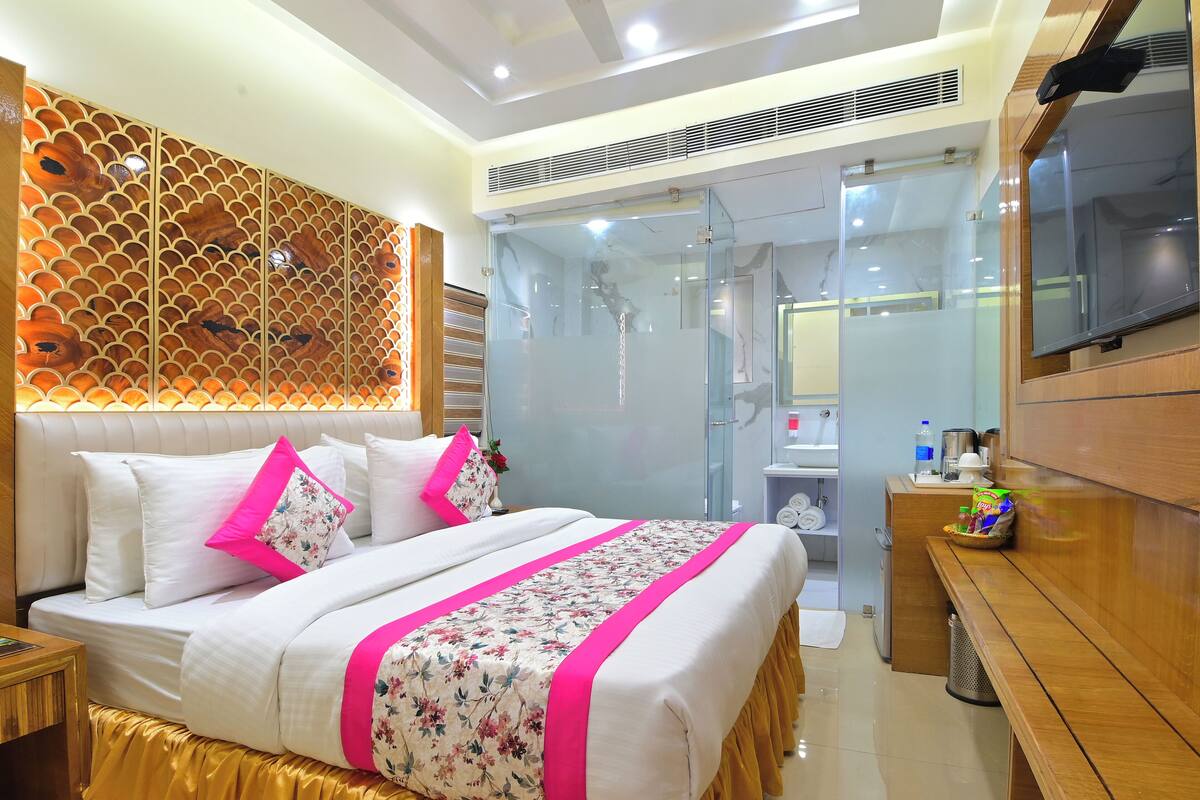 Quarto de hotel com cama, televisão, banheiro e escrivaninha.