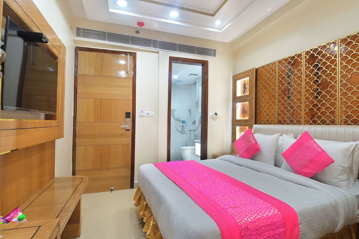 Quarto de hotel com uma cama grande, guarda-roupa de madeira e uma televisão sobre um suporte de madeira.