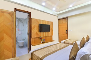 Een hotelkamer met een houten garderobe, een aan de muur bevestigde televisie, een badkamer met toilet en wastafel, en twee bedden met beddengoed met een patroon.