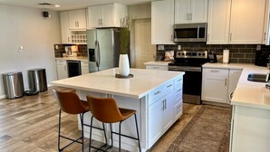 A modern kitchen with white cabinetry, a central island with bar stools, stainless steel appliances, and a decorative plant. - Arcadia oasis Heated Pool (Phoenix)