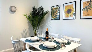 A dining table set with plates, glasses, and a bottle, surrounded by white chairs and a large plant. - St Mary's Sunscape (Huntingdon)