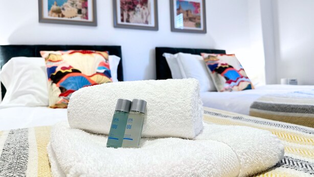 A neatly made bed with a white towel and two bottles of spa products, a colorful pillow, and framed pictures on the wall. - St Mary's Sunscape (Huntingdon)
