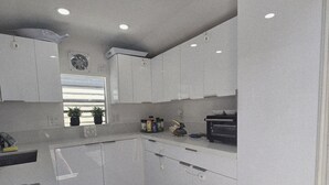 A modern kitchen with white cabinets, a countertop with appliances, and a window with blinds.