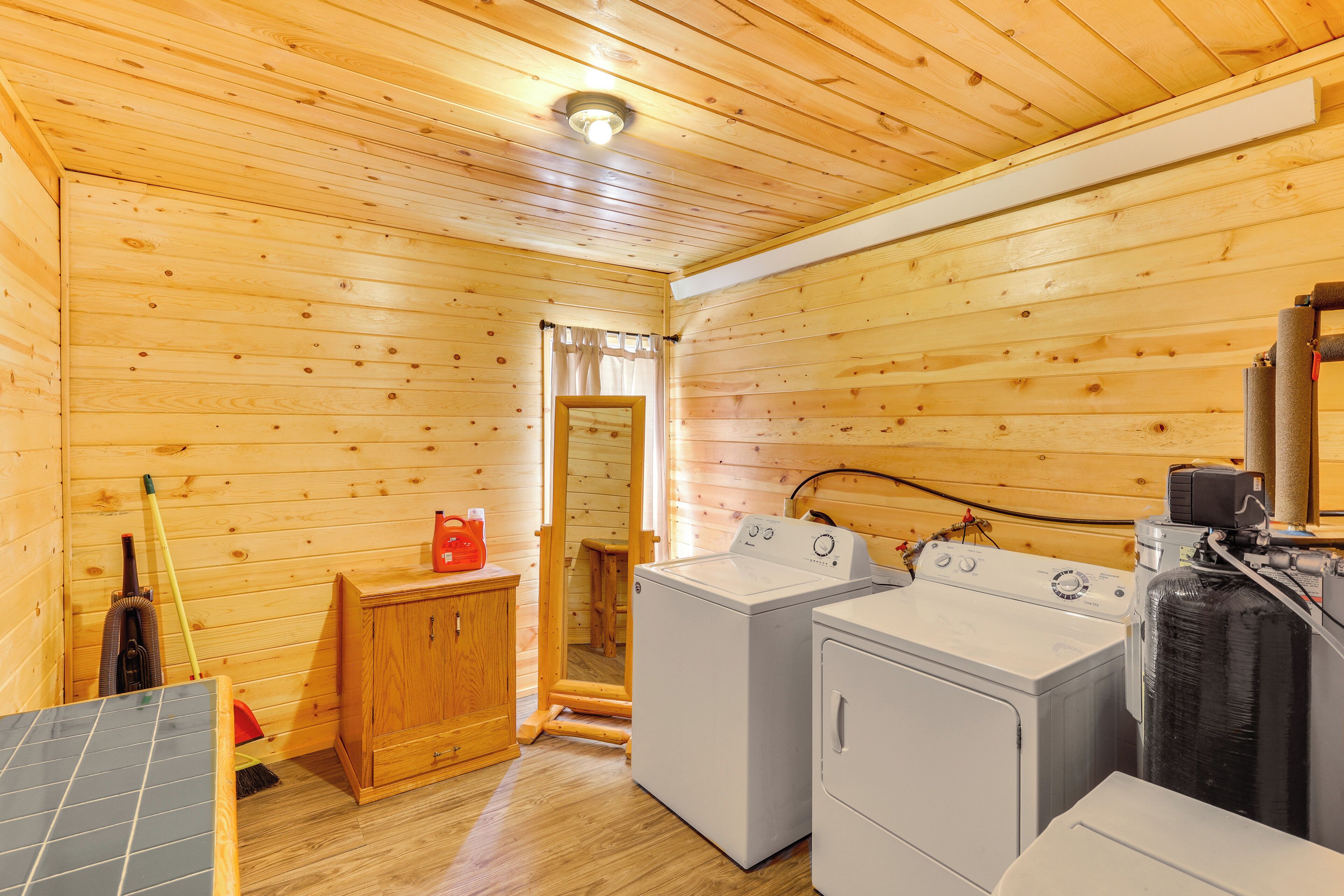 A laundry room with wooden walls and ceiling, two washing machines, a dryer, and a solar panel.