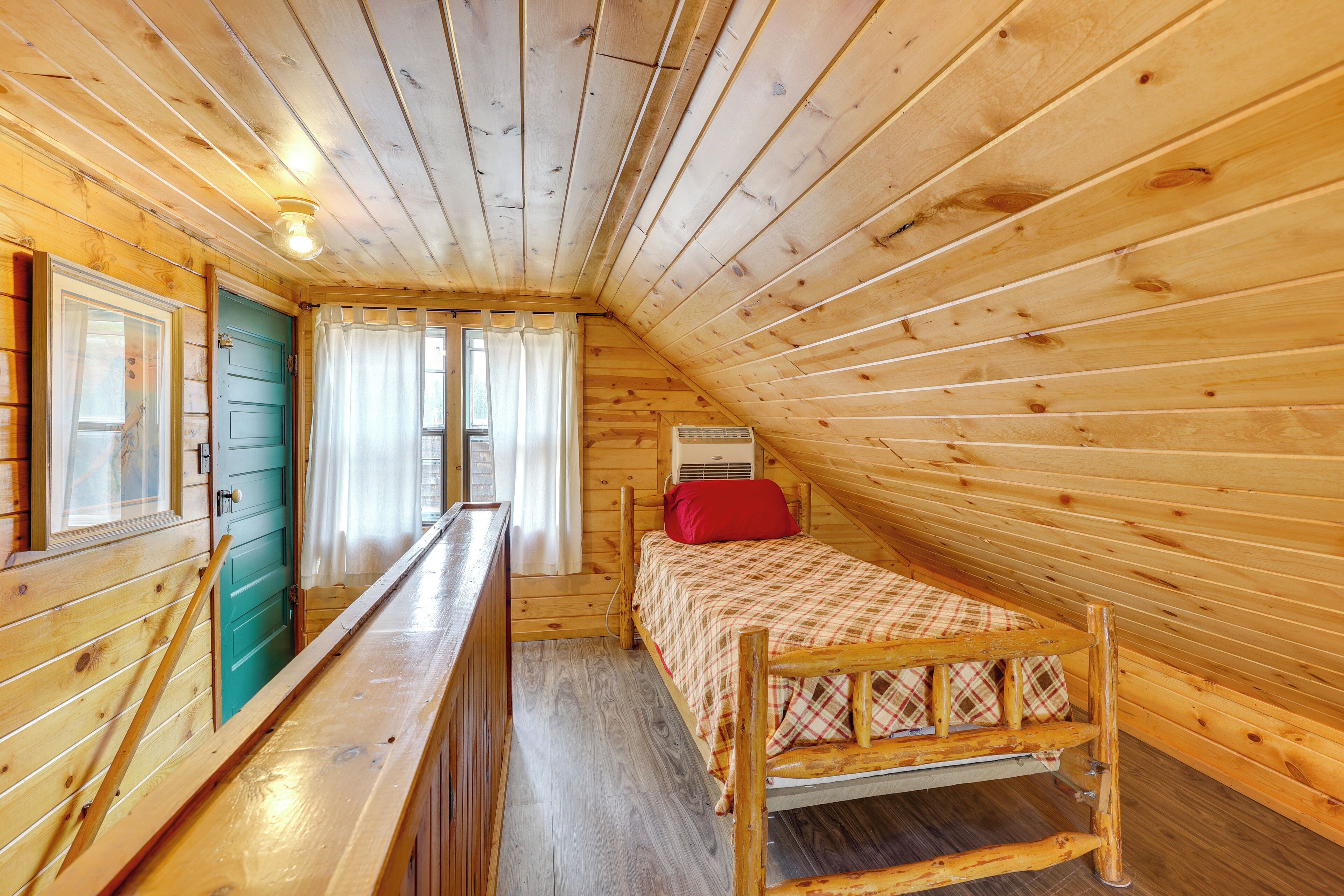 Una habitación de cabaña de madera con una cama, una ventana con cortinas y una puerta.