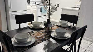 A dining area with a table set for four, surrounded by chairs, in a modern kitchen with white cabinets and appliances. - Eagle Stay 13- Eagle Pass (Eagle Pass)