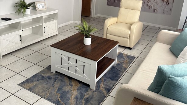 A modern living room with a flat-screen TV, a white entertainment unit, a beige armchair, a coffee table, and a large floral wall mural. - Eagle Stay 13- Eagle Pass (Eagle Pass)