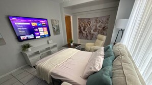 A modern hotel room with a bed, a sofa, a TV mounted on the wall, a desk, and a decorative wall panel. - Eagle Stay 13- Eagle Pass (Eagle Pass)
