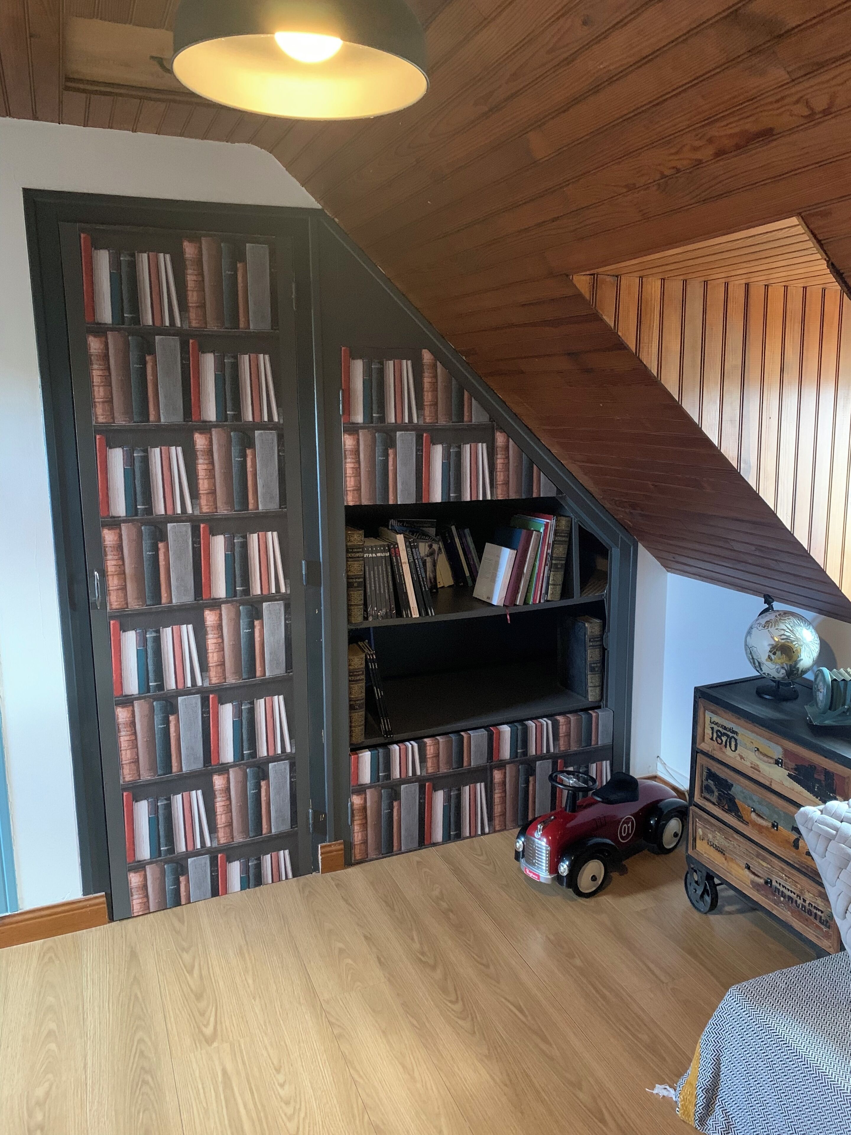 Une pièce avec un plafond en bois, une bibliothèque remplie de livres, un globe terrestre et une voiture jouet.