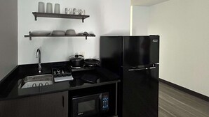 A compact kitchen with a black refrigerator, a microwave, a stove, and a sink. There are two shelves above the counter holding cups and bowls. - Studio 6 Pocatello, Id (Pocatello)