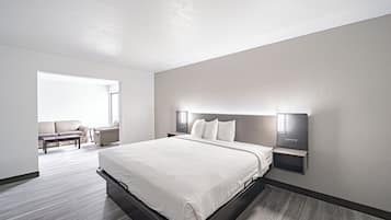 A modern hotel room with a large bed, a seating area with a sofa and armchairs, and a large window providing natural light.