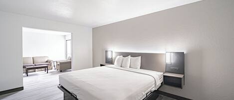 A modern hotel room with a large bed, a seating area with a sofa and armchairs, and a large window providing natural light.
