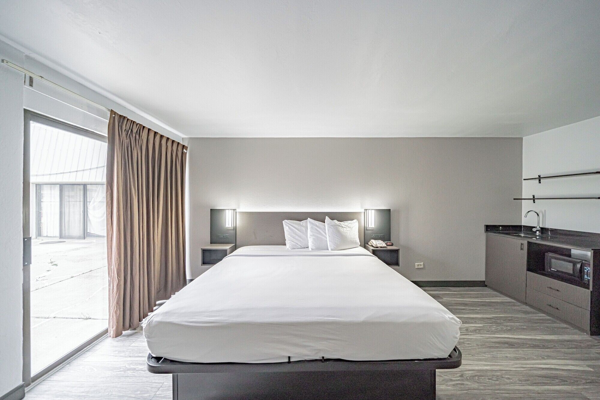 A modern hotel room with a large bed, a desk, a flat-screen TV, and a kitchenette.