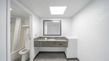 A bathroom with a white toilet, a shower with a white curtain, a granite countertop sink, and a mirror above it.