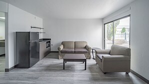 A modern living room with a sofa, a coffee table, and a kitchen area with a refrigerator. - Studio 6 Pocatello, Id (Pocatello)