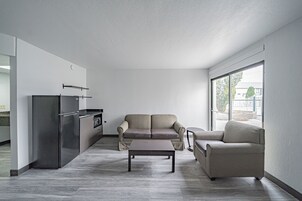 A modern living room with a sofa, a coffee table, and a kitchen area with a refrigerator.