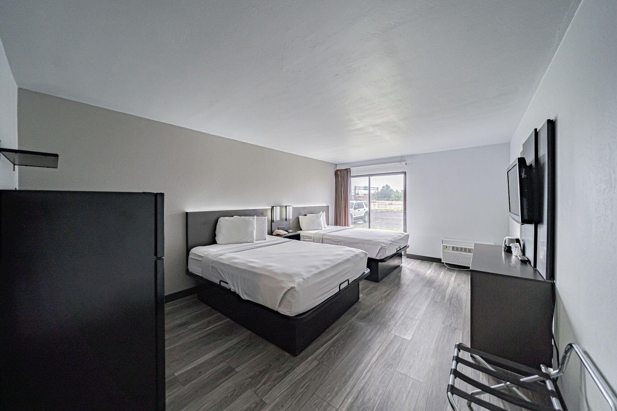 A modern hotel room with two beds, a flat-screen TV, and a large window.