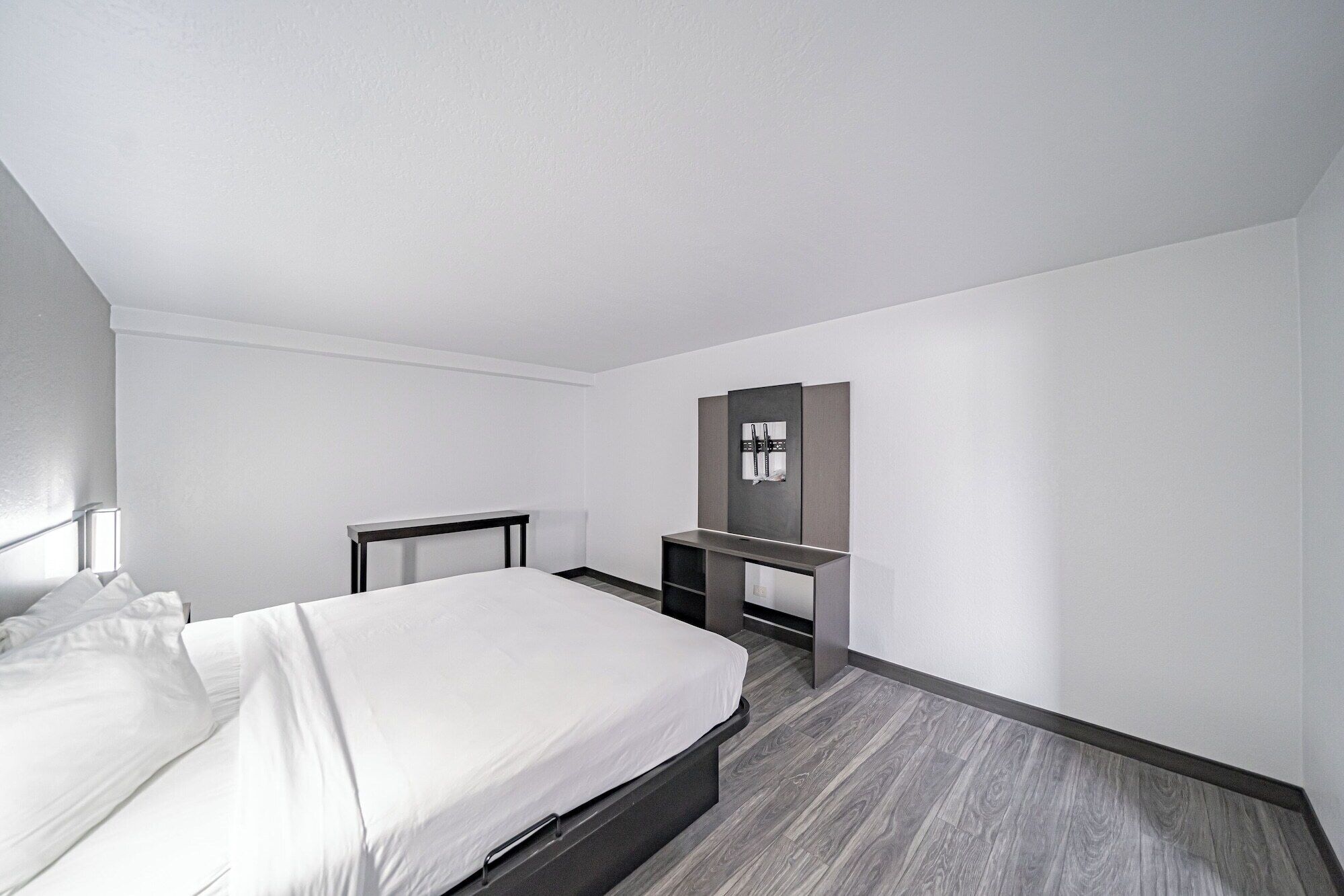 A hotel room with a bed, a desk, and a mirror on the wall.