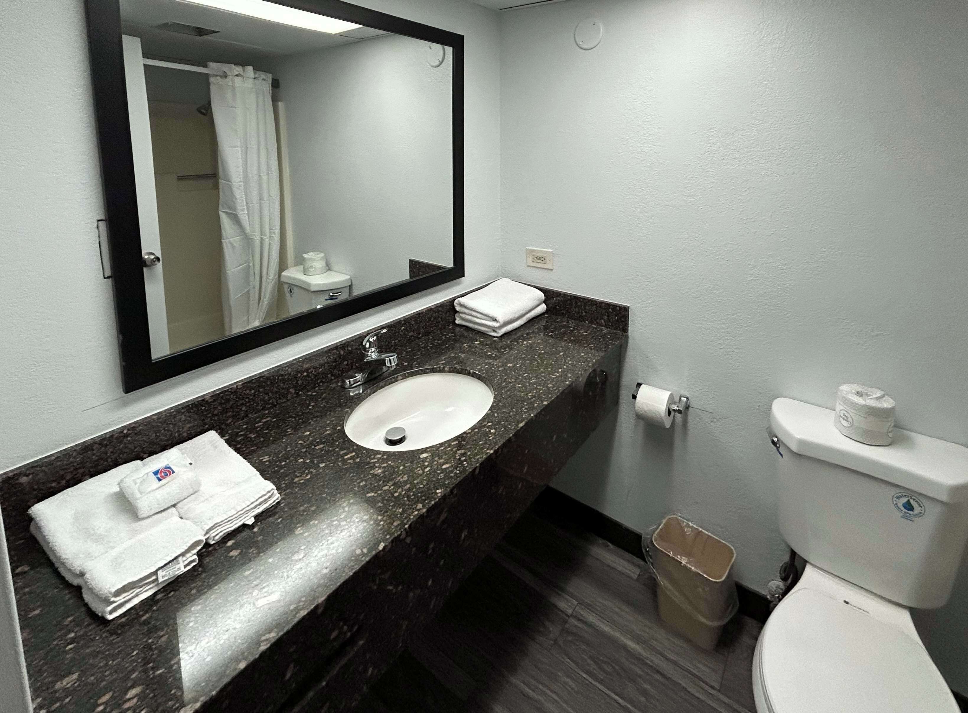 Une salle de bain équipée d’un lavabo, d’un miroir, de toilettes et d’une poubelle.