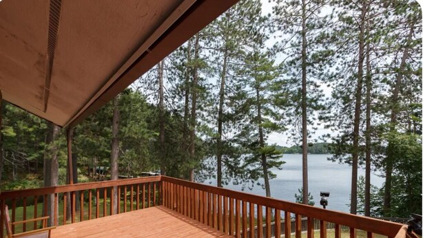 Una terraza de madera con barandilla que da a un lago rodeado de árboles.