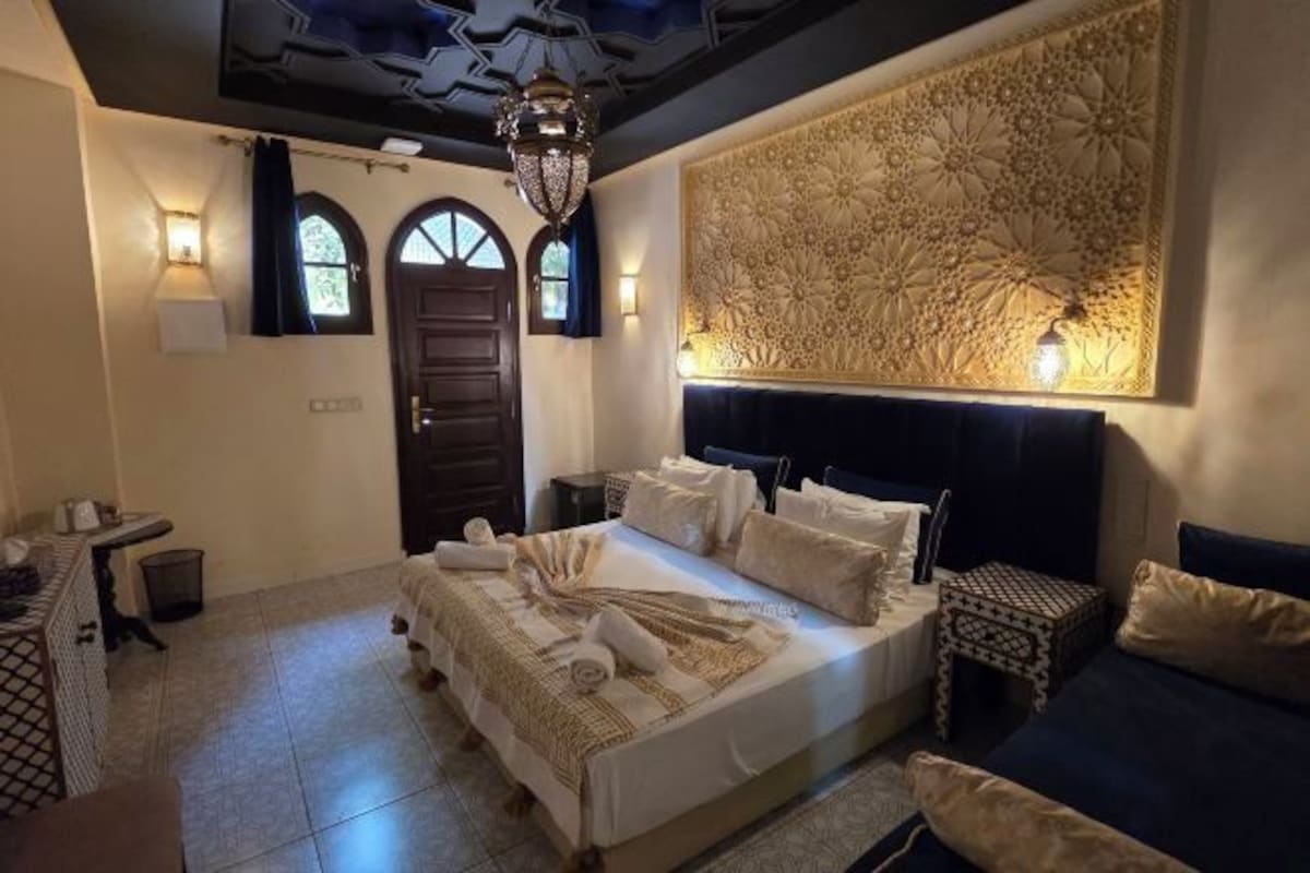 A hotel room with a large bed, a bedside table, a nightstand, and a wall-mounted lamp.