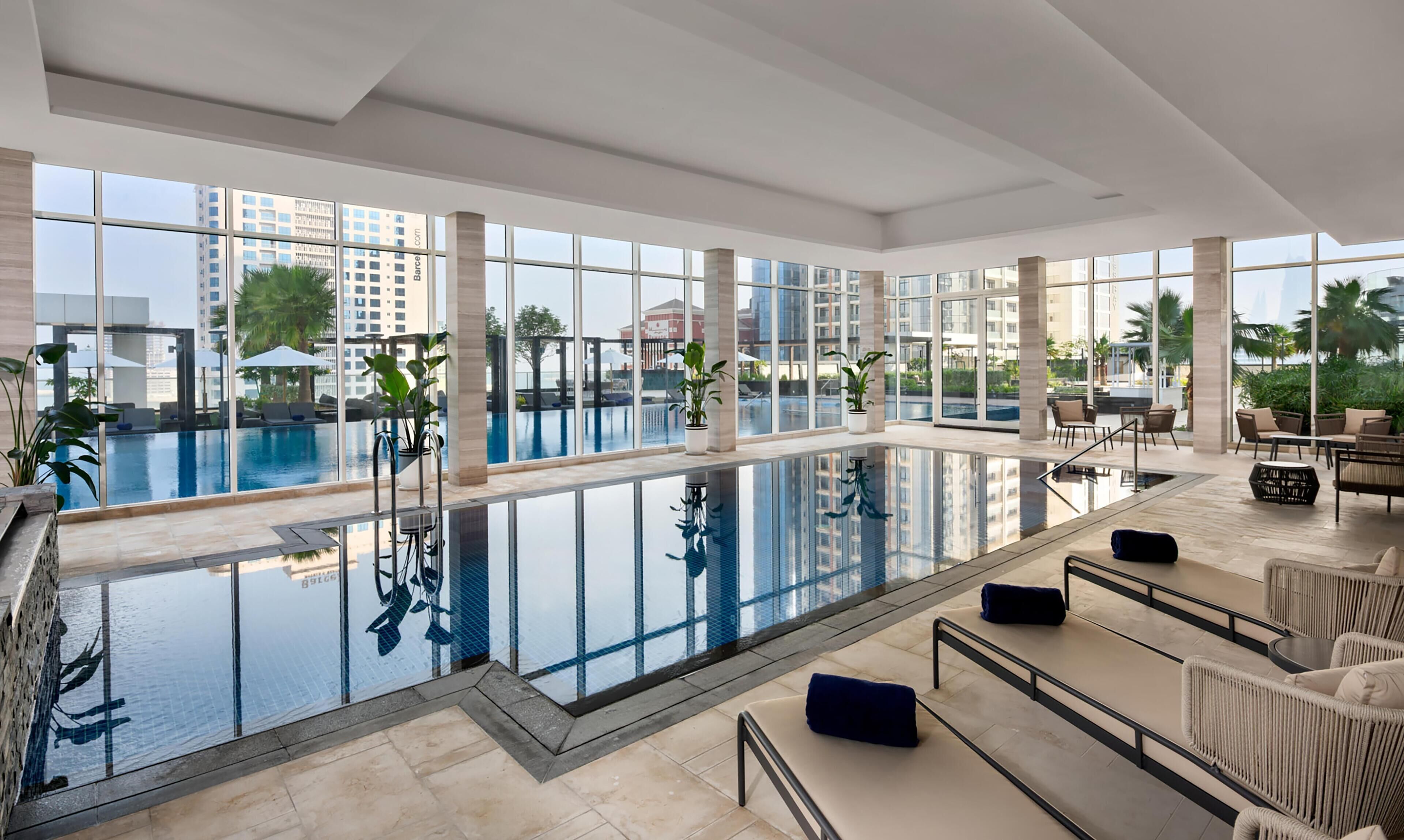 A modern indoor pool area with clear views of the surrounding buildings and a poolside seating area.