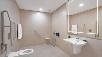 A modern bathroom with a toilet, sink, shower, and handrails.