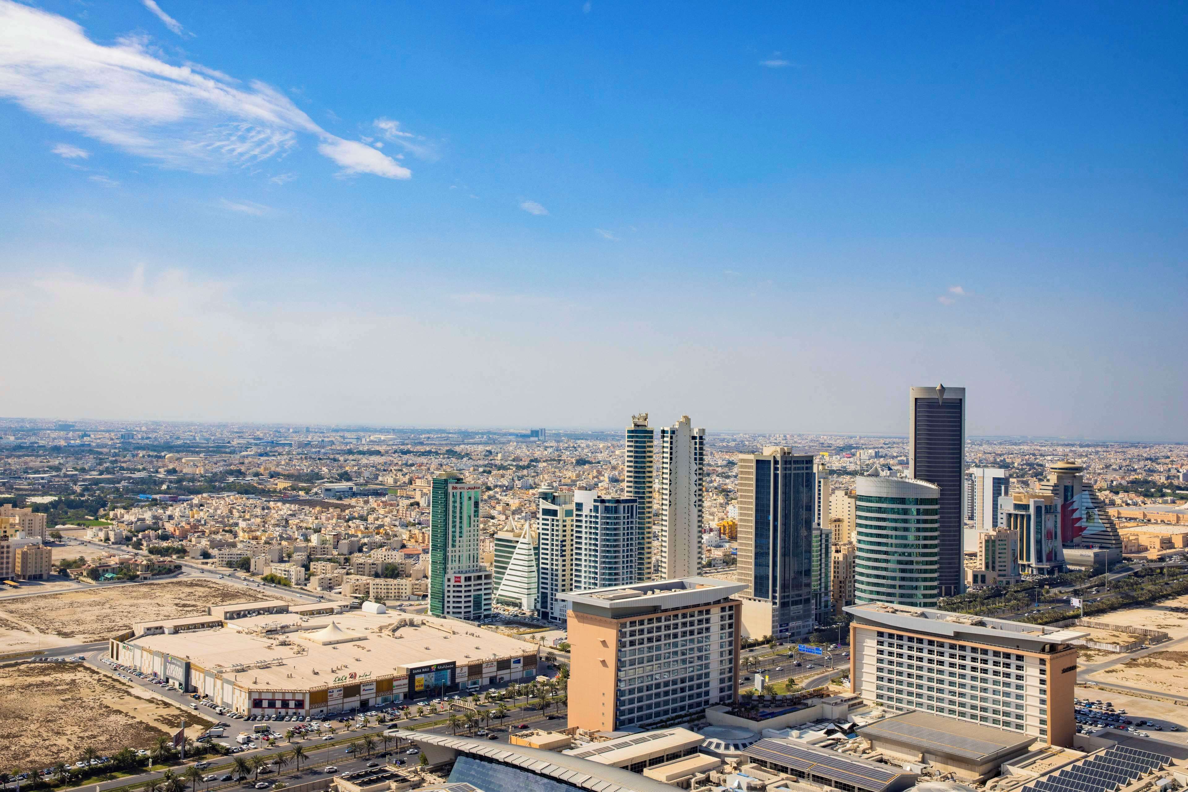 A cityscape with modern high-rise buildings, a large open plaza, and a clear blue sky.