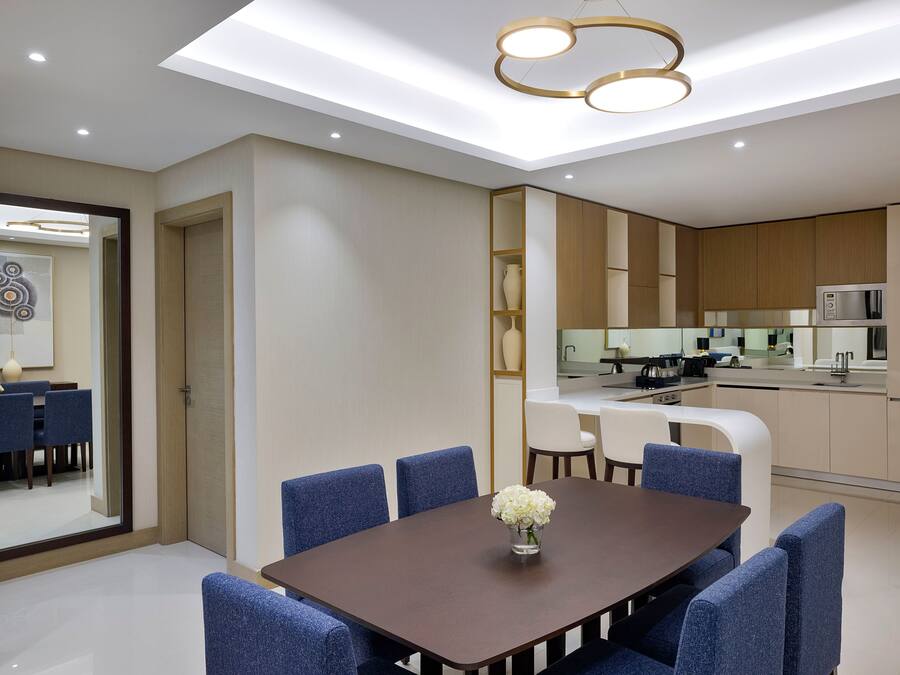 A modern dining area with a dark wooden table, blue upholstered chairs, and a vase of white flowers.
