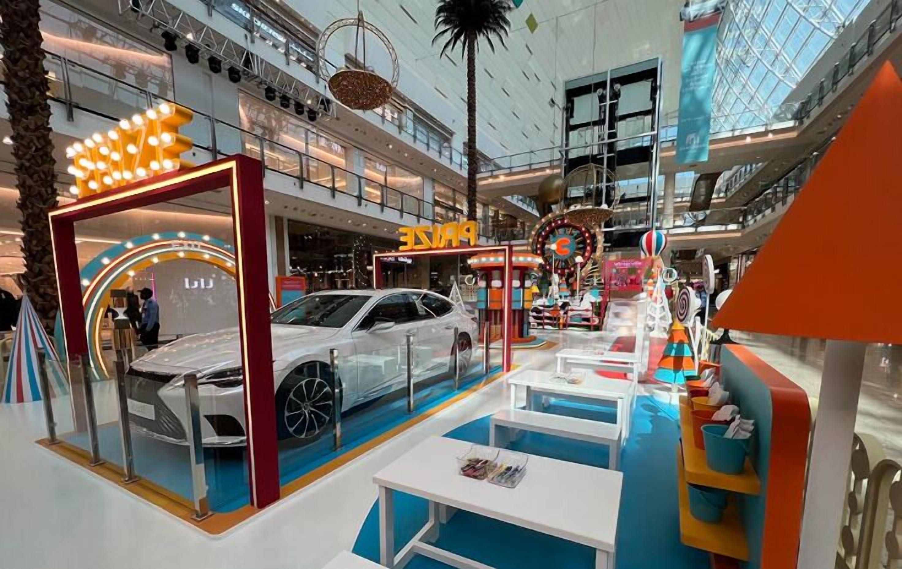 Un centre commercial moderne, situé à l’intérieur, qui propose un espace d’exposition de voitures, un magasin « PINK » et une grande roue.