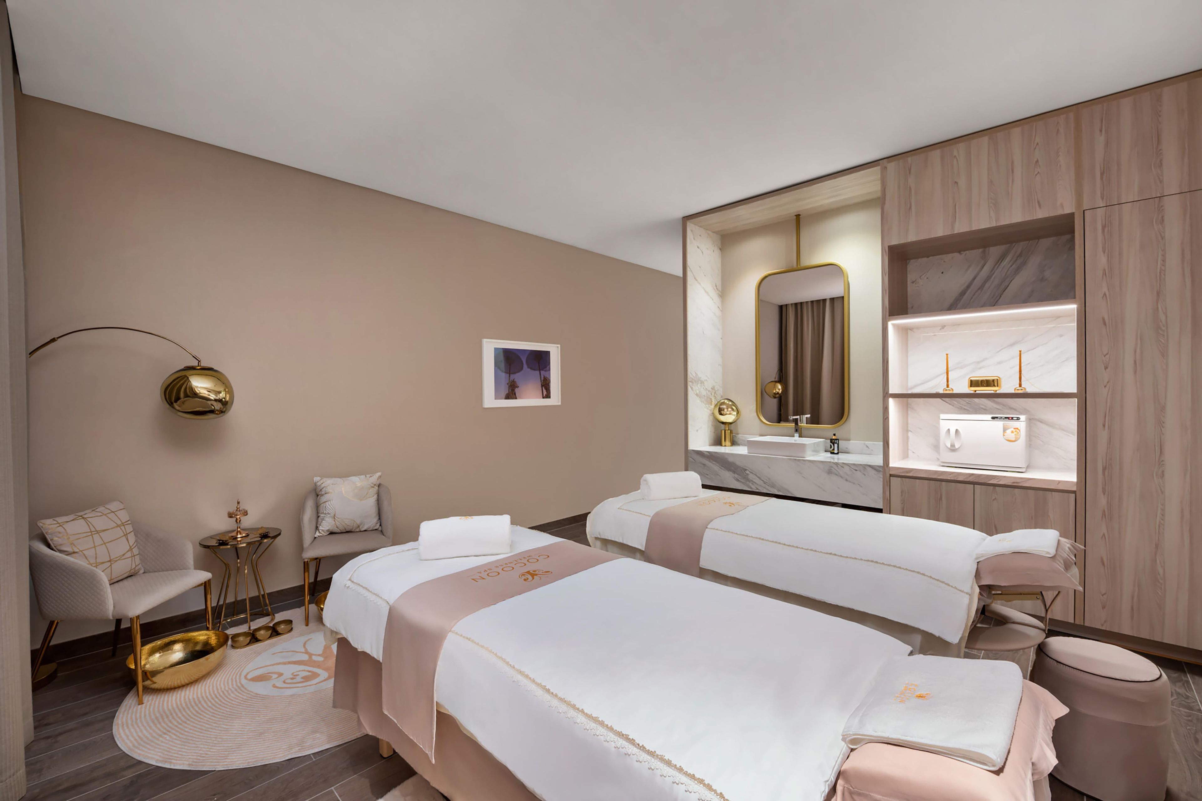 Habitación de hotel con dos camas, una zona de estar con una silla y una mesa, un tocador con espejo y una ventana con vistas.