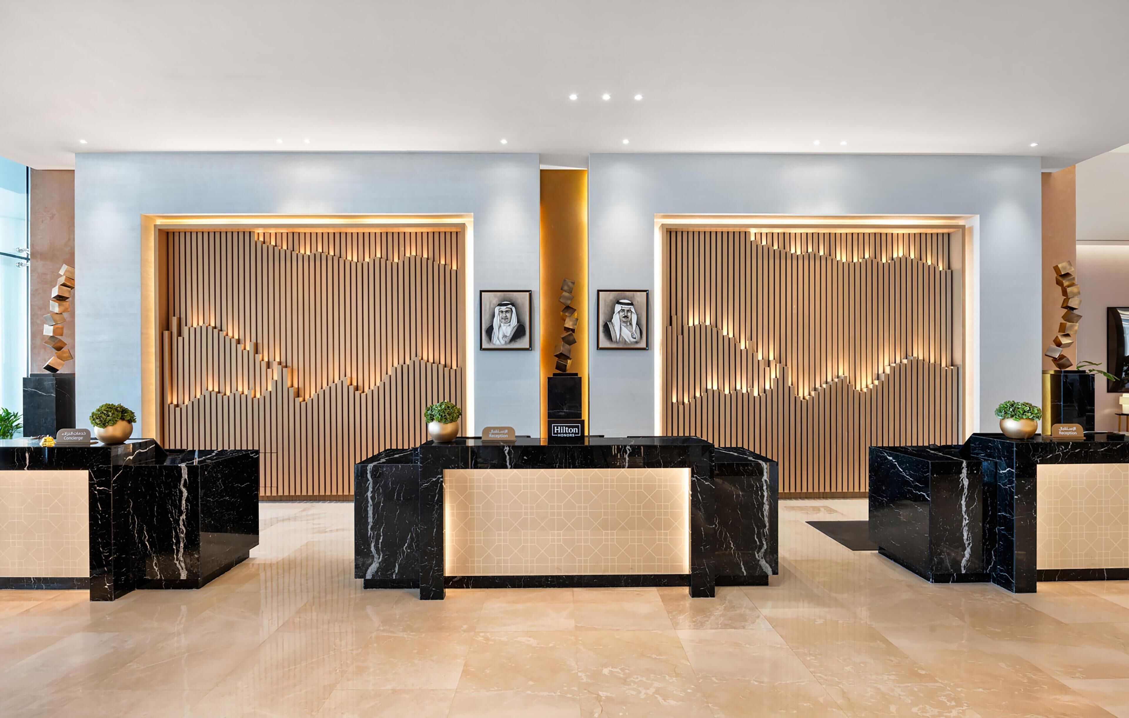 A modern hotel reception area with marble counters, vertical wooden panels, and framed artwork.