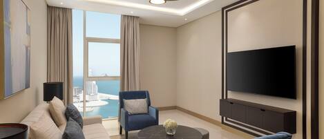 A modern living room with a sofa, armchairs, a coffee table, a TV, and a large window with a view of a cityscape.