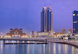 A waterfront cityscape with modern high-rise buildings, including a prominent Hilton hotel.