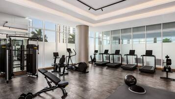 Un gimnasio moderno con equipo de ejercicio, ventanas amplias y vistas a palmeras.