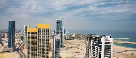 A high-rise building with a distinctive yellow section, surrounded by other tall buildings, a beach, and a clear sky.