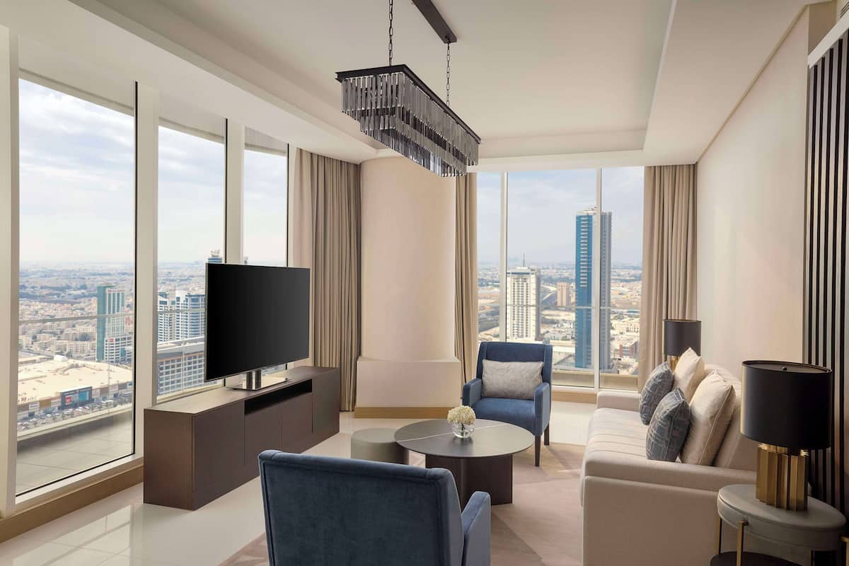 Una sala de estar moderna con un televisor grande, asientos cómodos, una mesa de centro y vistas a la ciudad.