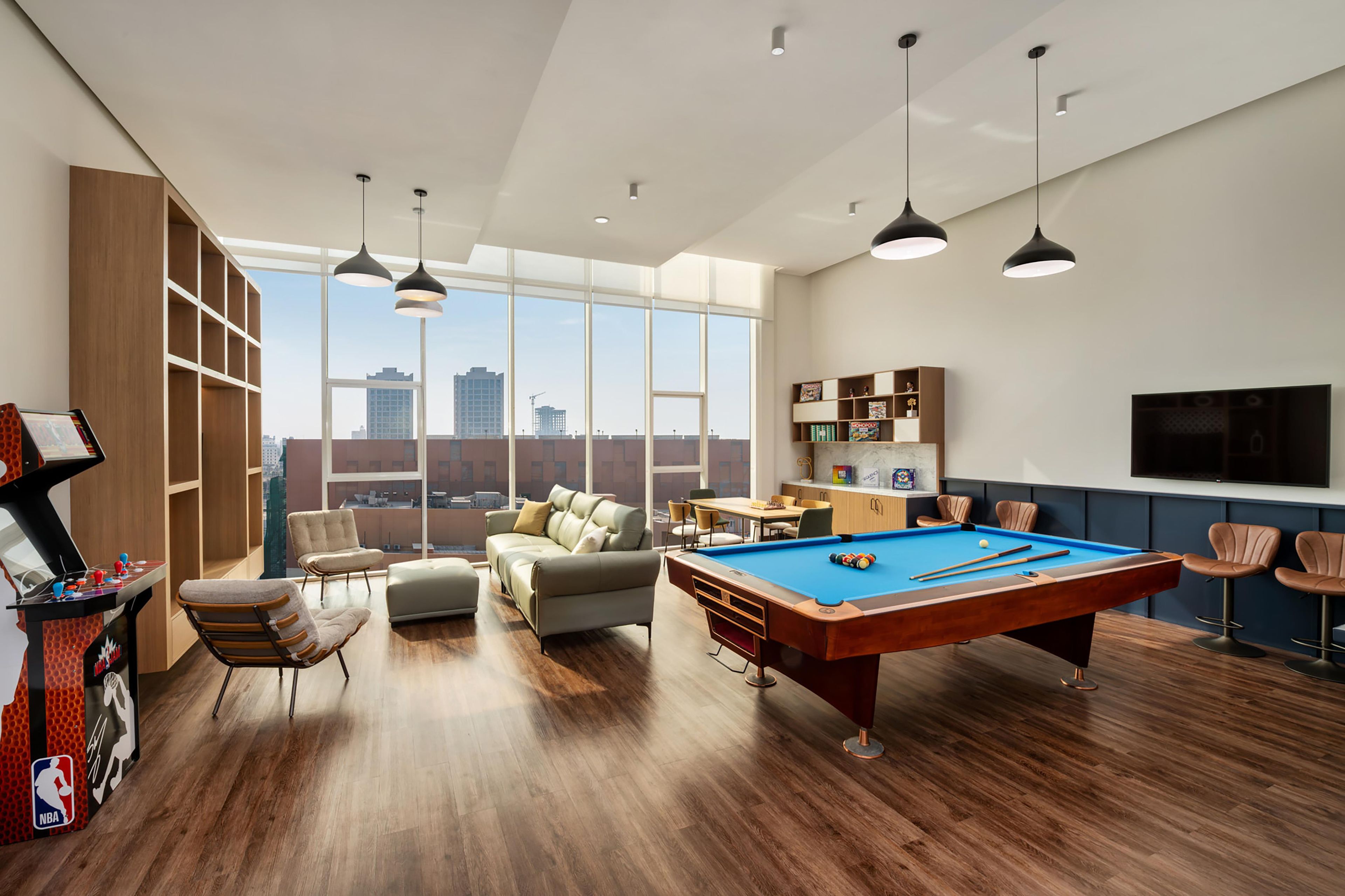 Una sala moderna con mesa de billar, asientos cómodos y un amplio ventanal con vista a la ciudad.