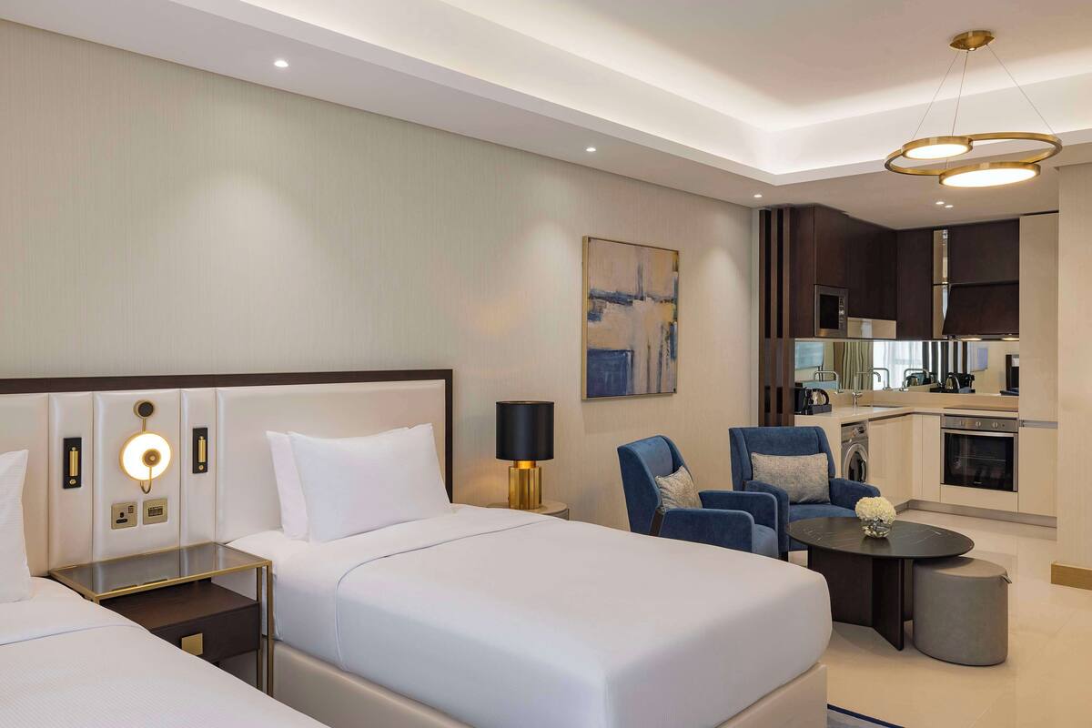 Una habitación de hotel con una cama grande, un escritorio, una silla, una mesita y una kitchenette.