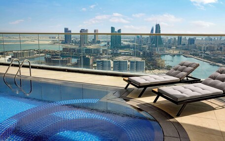 A rooftop pool with a city view, lounge chairs, and a glass railing.