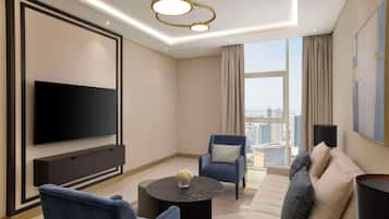 A modern living room with a flat-screen TV, a sofa, two armchairs, a coffee table, and a large window with a city view.