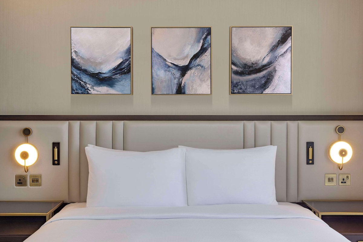 Ein Hotelzimmer mit einem Bett, zwei Nachttischen und drei abstrakten Bildern an der Wand.