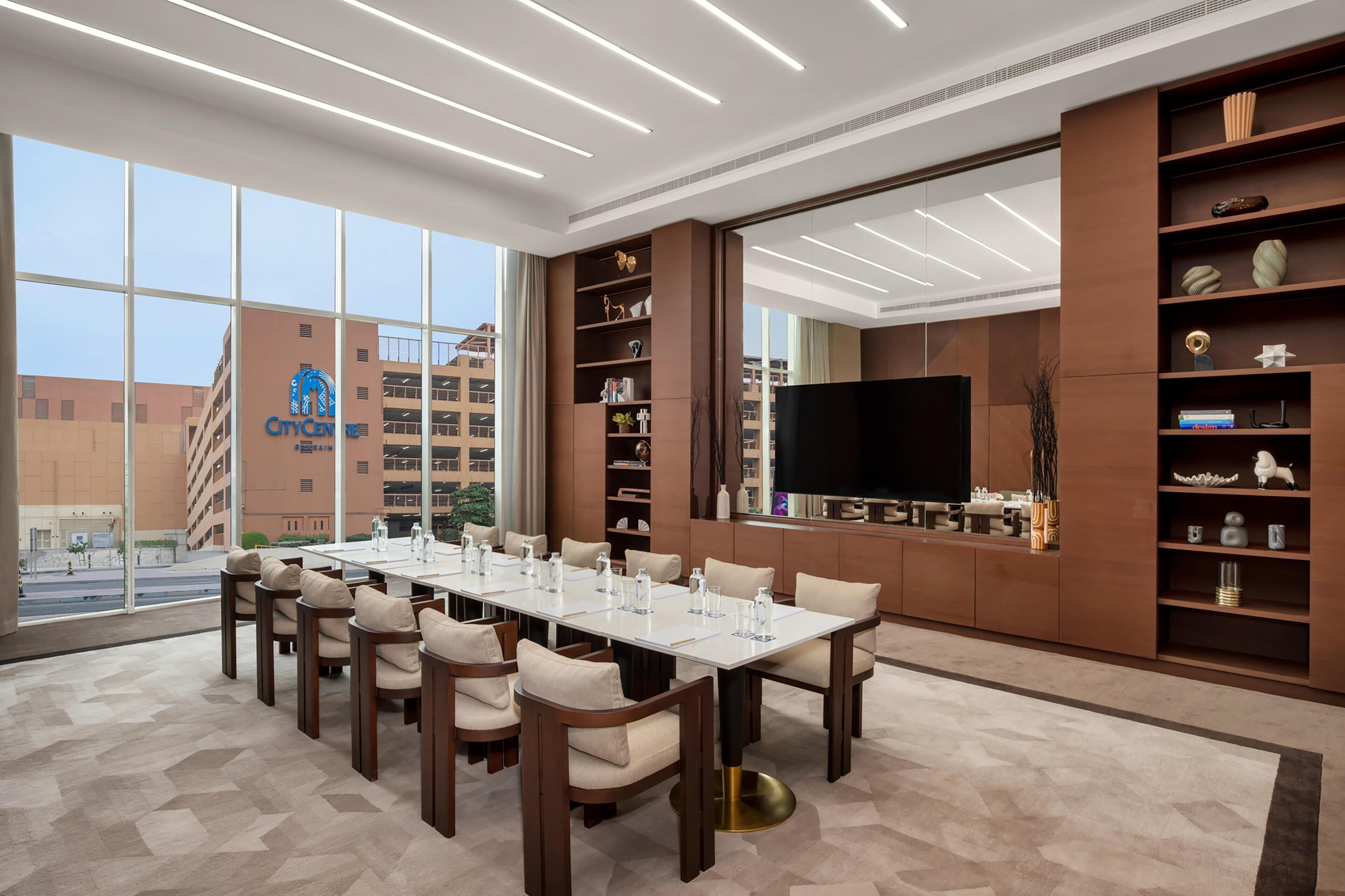 A conference room with a long table, chairs, a TV, and shelves with decorative items.