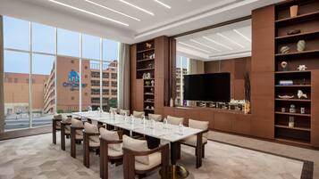 A conference room with a long table, chairs, a TV, and shelves with decorative items.