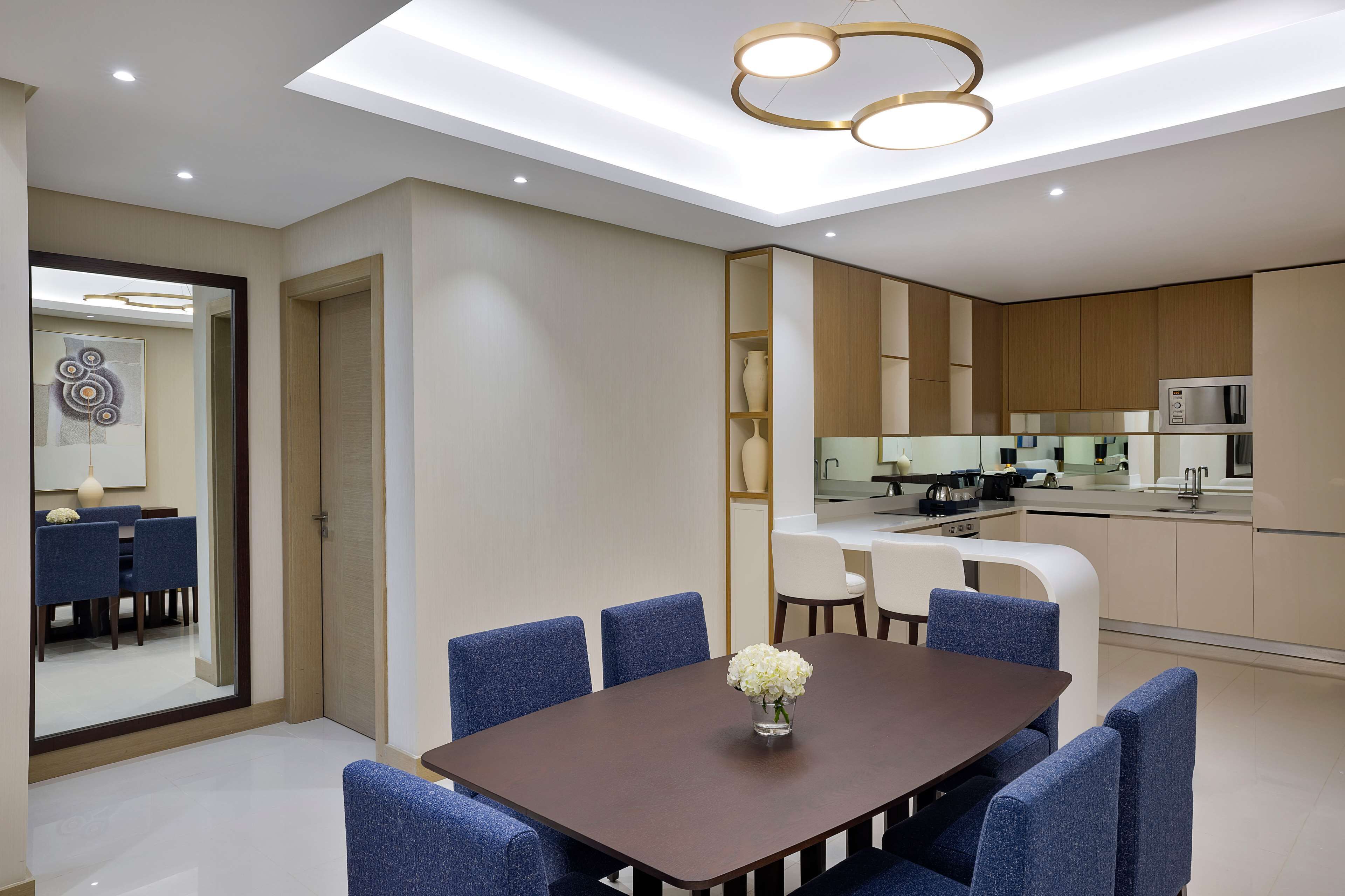 A modern dining area with a rectangular table, blue upholstered chairs, and a vase of flowers.