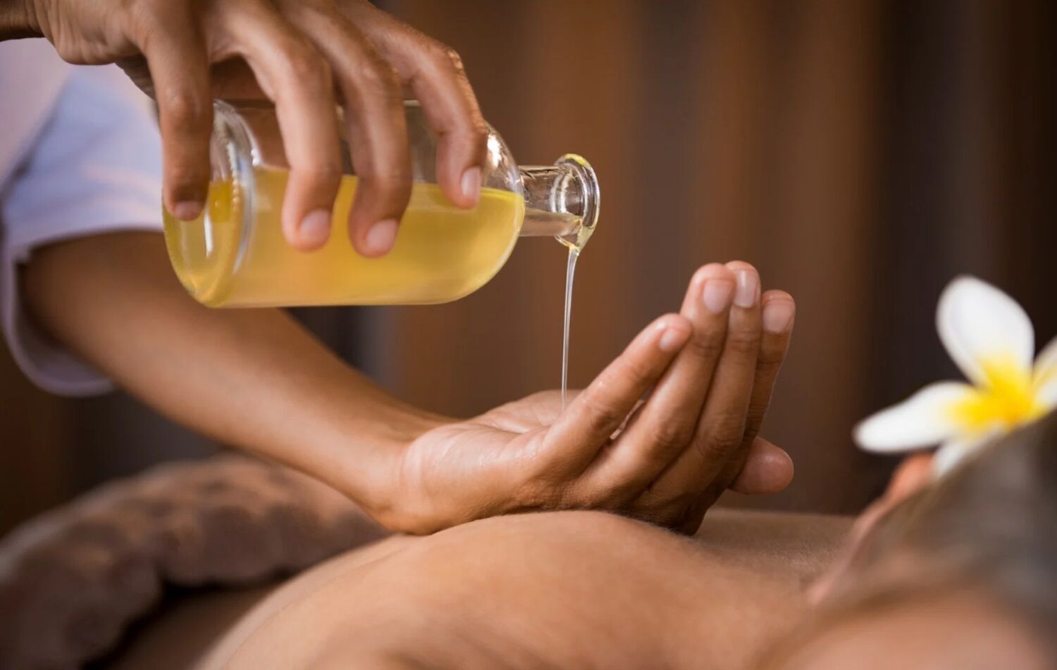 A person receiving a massage with a bottle of oil being poured onto their hand.