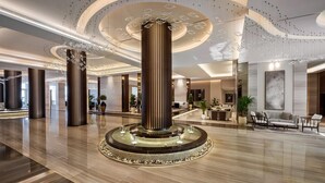 Een ruime lobby met een centrale kolom, een zithoek en een receptiebalie.