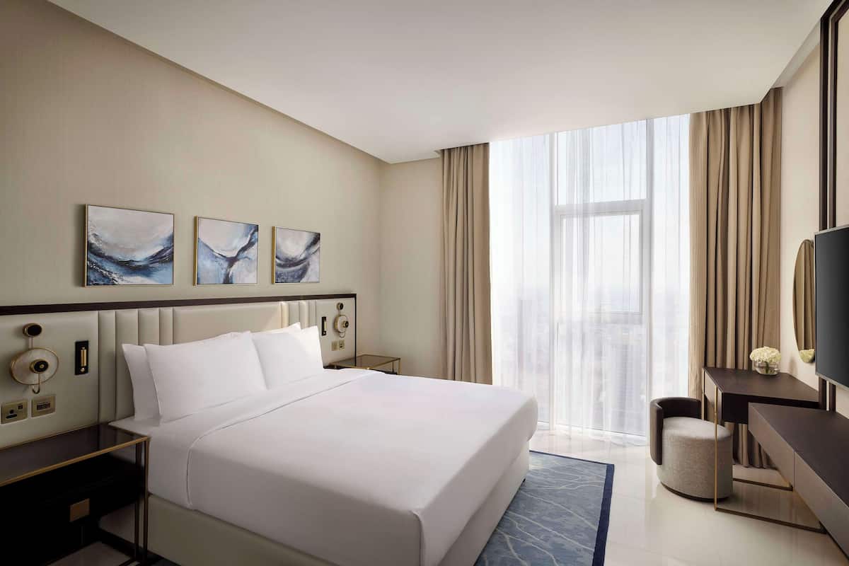 Habitación de hotel con una cama grande, un escritorio, una silla, un televisor y obras de arte en la pared.