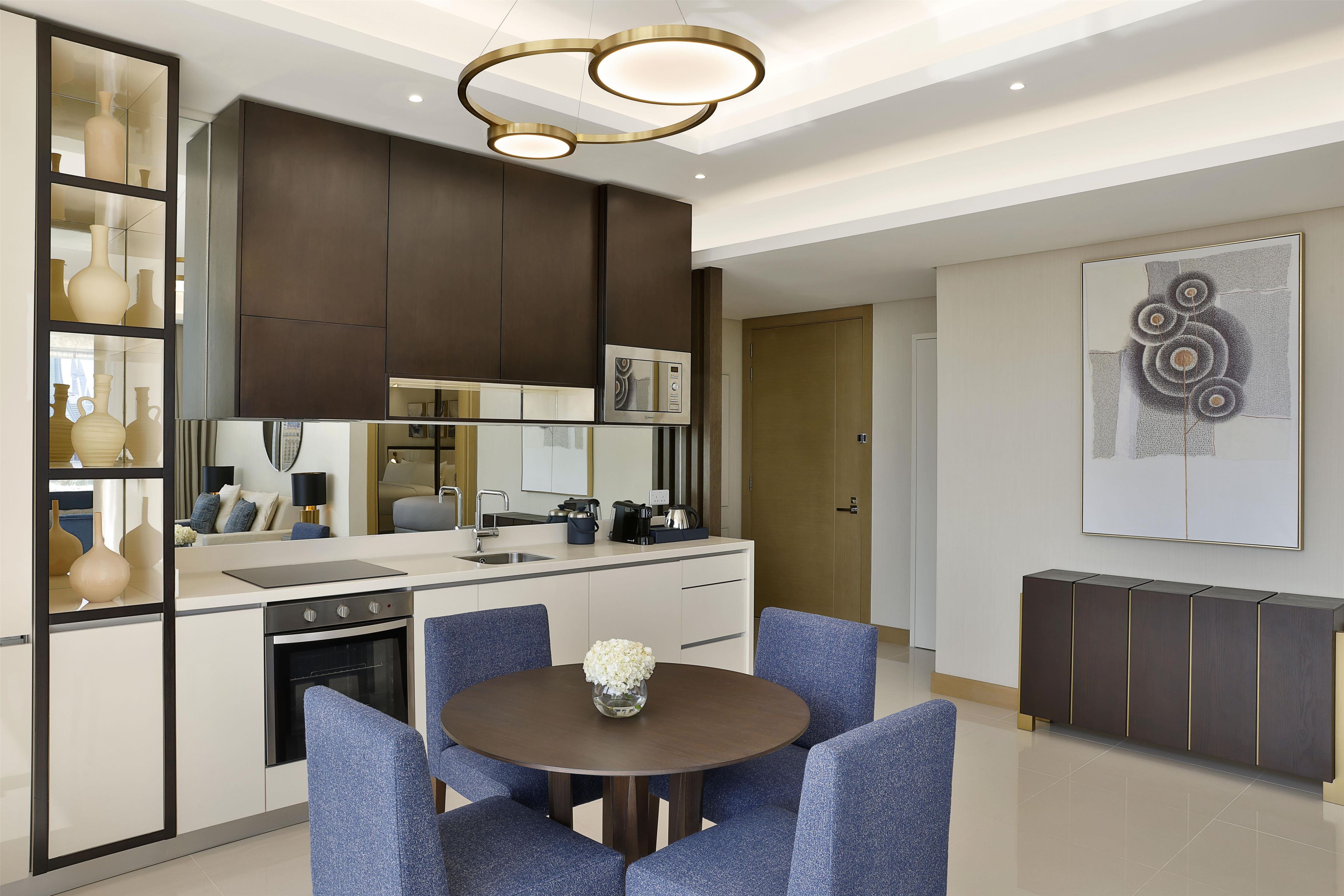 A modern kitchen with built-in appliances, a dining area with blue upholstered chairs, and a decorative wall piece.